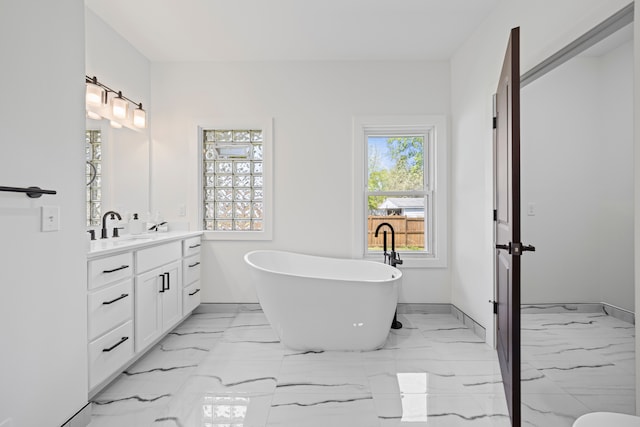 full bath featuring vanity, a soaking tub, marble finish flooring, and baseboards
