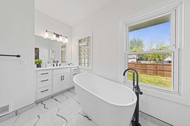 bathroom featuring healthy amount of natural light, vanity, a soaking tub, and marble finish flooring