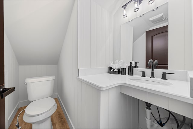 half bathroom with a sink, toilet, vaulted ceiling, and wood finished floors