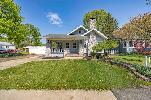 view of front of house with stone siding, a chimney, a porch, and concrete driveway