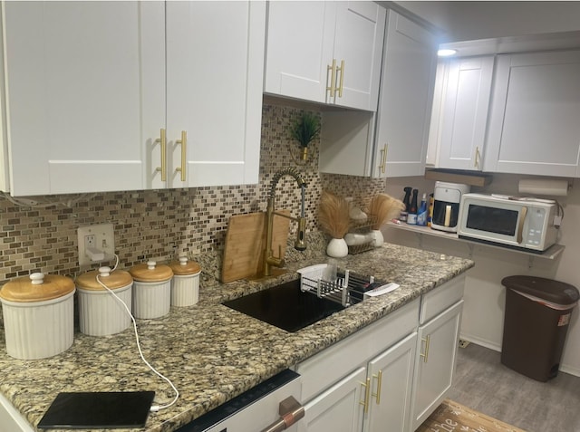 kitchen with white microwave, white cabinetry, a sink, and light stone countertops