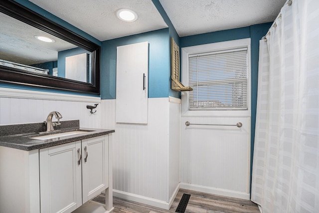 full bathroom featuring wood finished floors, a textured ceiling, a wainscoted wall, vanity, and baseboards