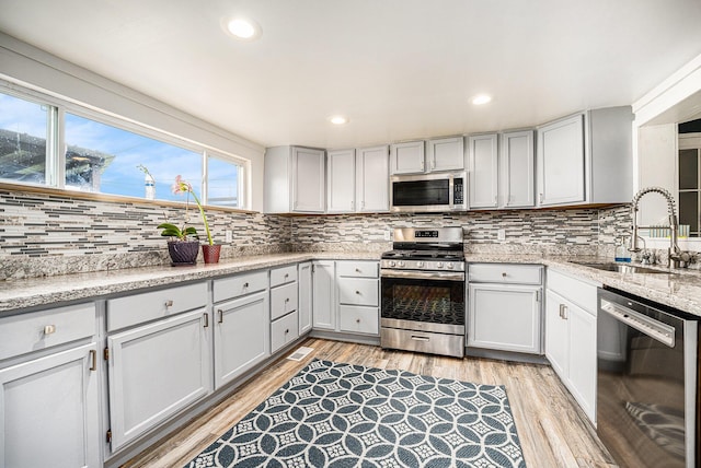 kitchen featuring stainless steel appliances, a sink, backsplash, light wood-style flooring, and recessed lighting
