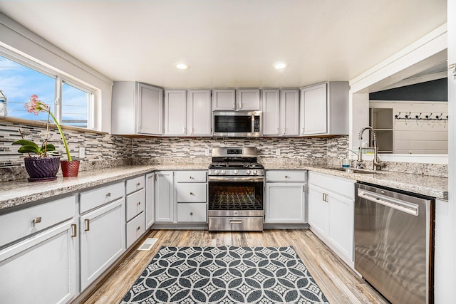 kitchen featuring appliances with stainless steel finishes, a sink, tasteful backsplash, light wood-style flooring, and recessed lighting