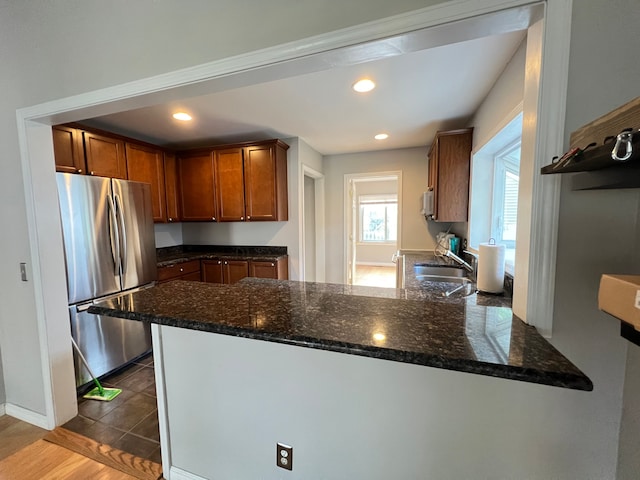 kitchen with freestanding refrigerator, a peninsula, recessed lighting, dark stone counters, and a sink