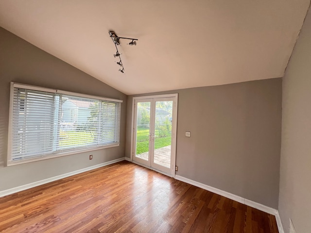 empty room with lofted ceiling, track lighting, baseboards, and wood finished floors