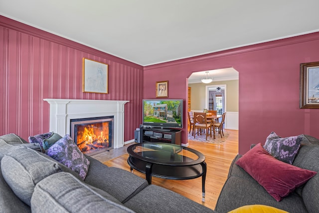 living area featuring ornamental molding, arched walkways, a fireplace with flush hearth, wood finished floors, and a wainscoted wall