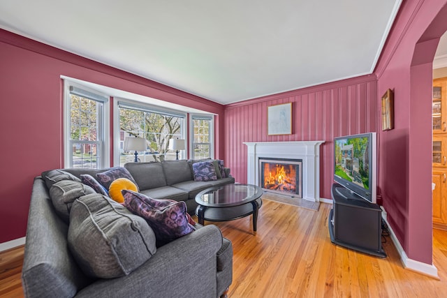 living area with a lit fireplace, ornamental molding, light wood finished floors, and baseboards