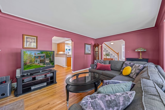 living area featuring arched walkways, wood finished floors, crown molding, stairway, and baseboards