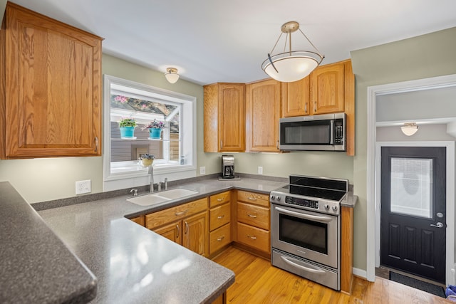 kitchen featuring stainless steel appliances, a sink, light wood finished floors, decorative light fixtures, and dark countertops