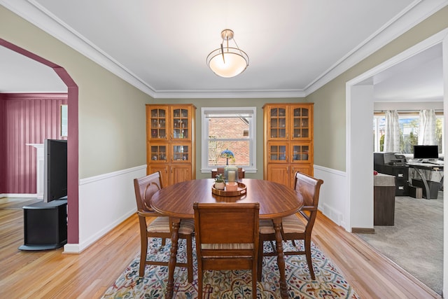 dining room featuring wainscoting, light wood finished floors, ornamental molding, and arched walkways
