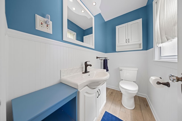 half bathroom featuring a wainscoted wall, healthy amount of natural light, wood finished floors, toilet, and vanity