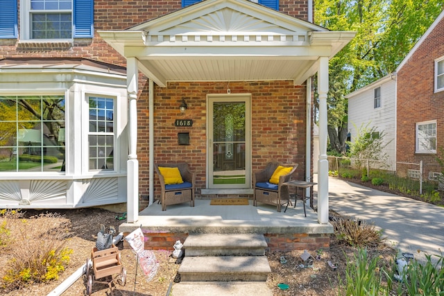view of exterior entry with a porch, brick siding, fence, and a chimney