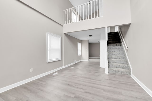 unfurnished living room featuring stairway, wood finished floors, baseboards, and a high ceiling