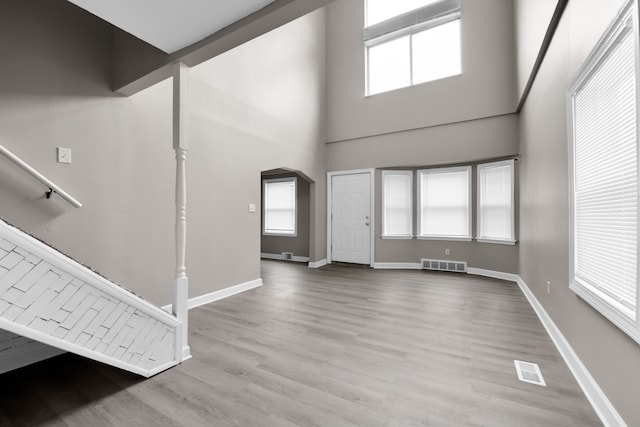 foyer with baseboards, wood finished floors, arched walkways, and a towering ceiling