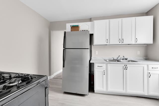 kitchen with freestanding refrigerator, a sink, light wood-style floors, and white cabinets