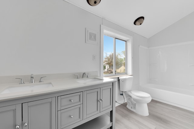 bathroom with toilet, wood finished floors, vaulted ceiling, and double vanity