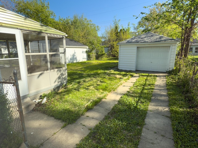 view of green lawn featuring an outdoor structure, a garage, driveway, and a sunroom