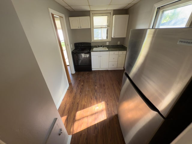 kitchen with black range with electric stovetop, freestanding refrigerator, a paneled ceiling, dark countertops, and white cabinetry