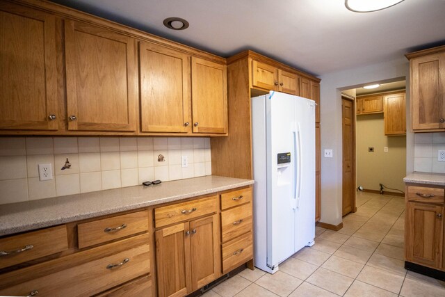 kitchen featuring white fridge with ice dispenser, brown cabinetry, decorative backsplash, and light tile patterned floors