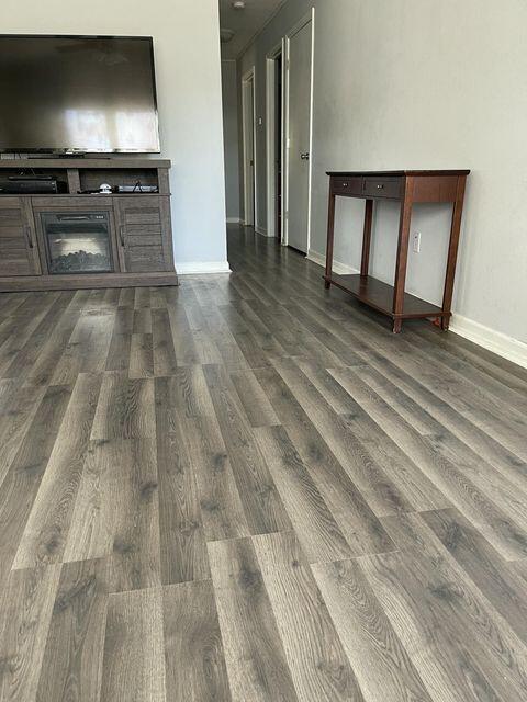 unfurnished living room with dark wood finished floors, baseboards, and a glass covered fireplace