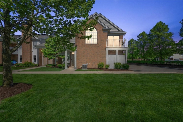 view of front of home with brick siding, central AC, a front yard, and a balcony