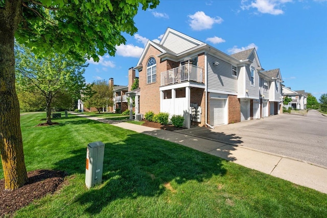 view of property exterior featuring brick siding, a balcony, a lawn, asphalt driveway, and a garage