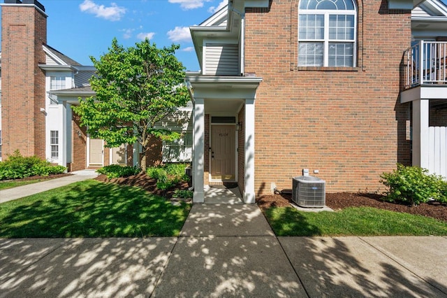 entrance to property featuring brick siding, central AC unit, and a balcony