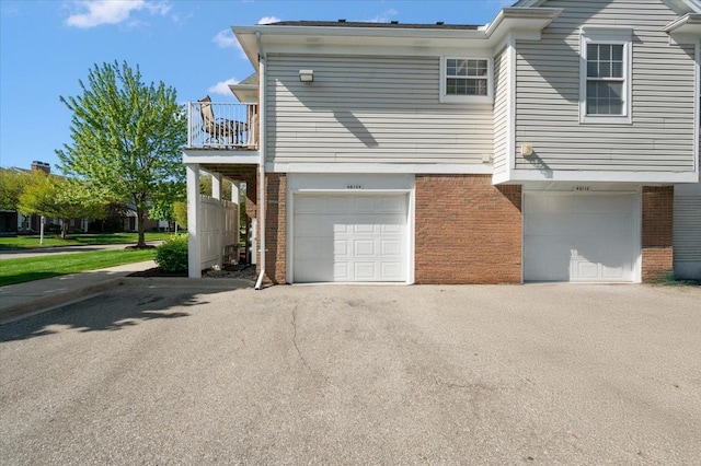 view of side of home with brick siding, a balcony, an attached garage, and driveway