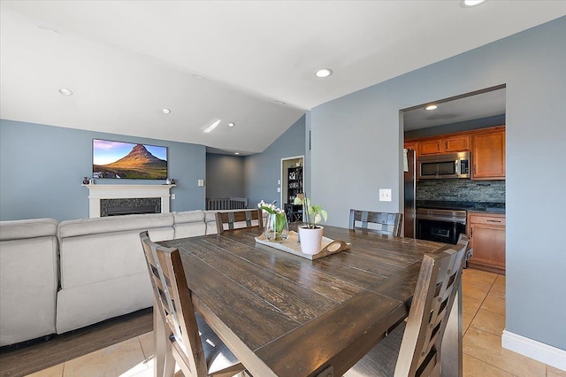 dining room with lofted ceiling, light tile patterned flooring, a fireplace, and recessed lighting