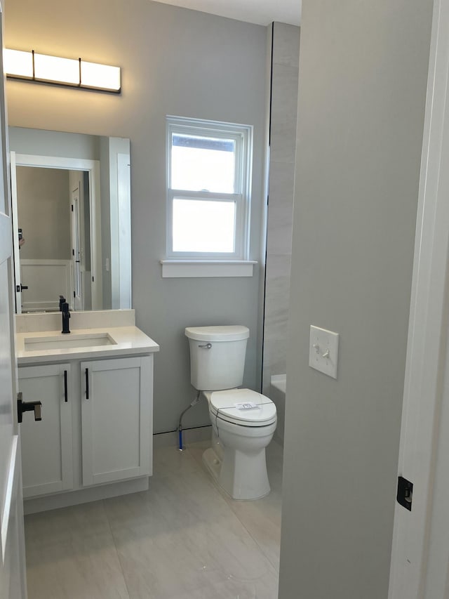 bathroom featuring toilet, vanity, tile patterned floors, baseboards, and a bath