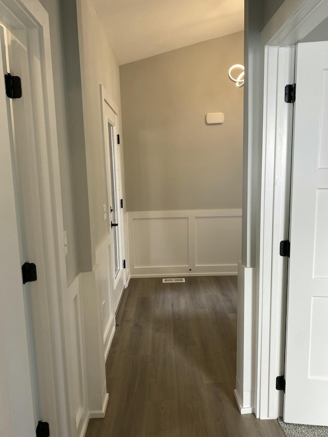 corridor with dark wood-style flooring, a wainscoted wall, and a decorative wall
