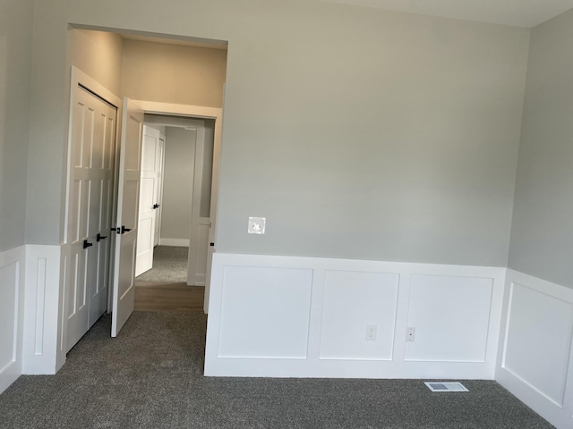 unfurnished room with dark colored carpet, a decorative wall, and wainscoting
