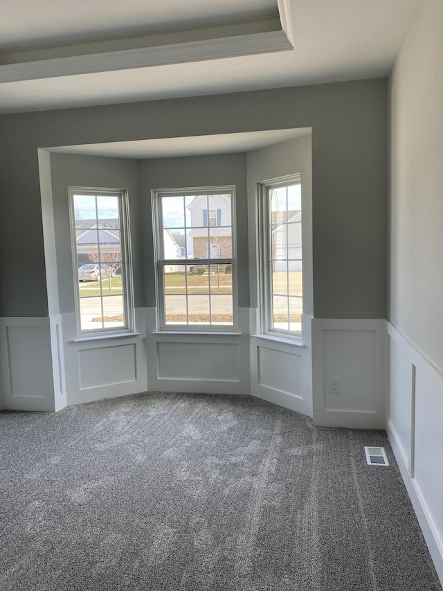 empty room with a wainscoted wall, dark carpet, a decorative wall, and plenty of natural light