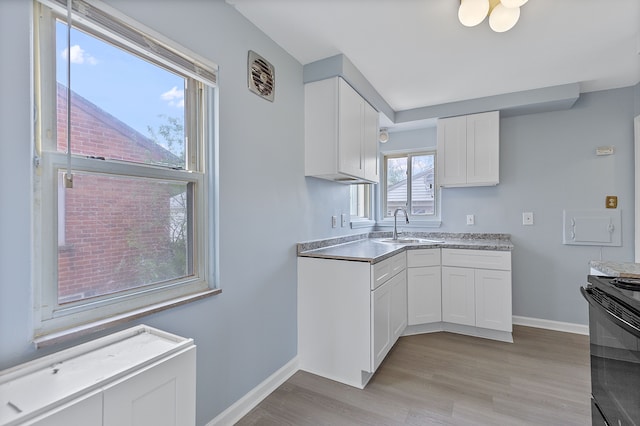 kitchen featuring a sink, black / electric stove, light wood-type flooring, white cabinetry, and baseboards