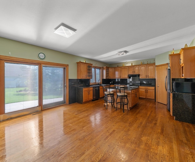 kitchen featuring appliances with stainless steel finishes, dark countertops, a breakfast bar area, glass insert cabinets, and a sink