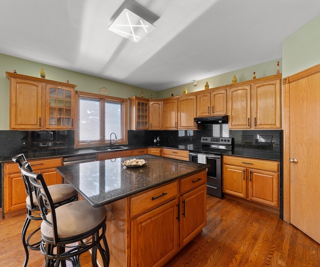 kitchen featuring stainless steel electric range oven, a breakfast bar area, glass insert cabinets, and backsplash