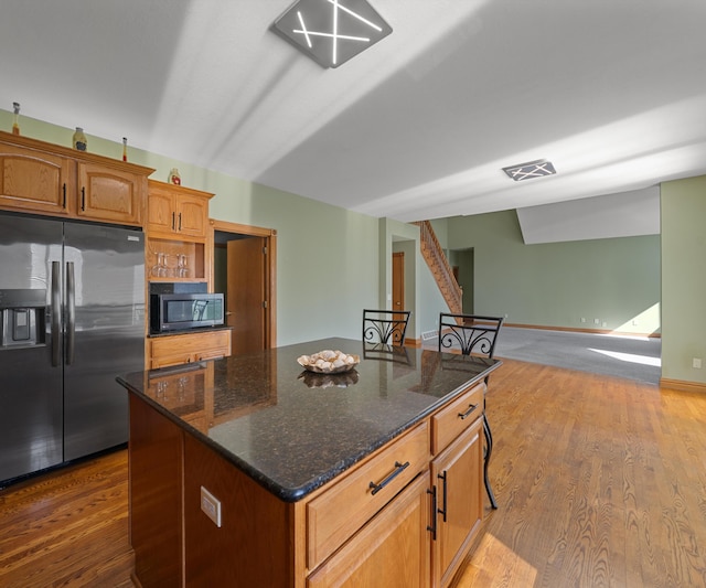 kitchen featuring stainless steel fridge with ice dispenser, dark stone counters, a kitchen island, and dark wood-type flooring
