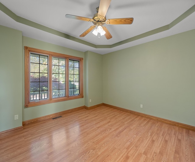 spare room featuring a tray ceiling, light wood-style floors, baseboards, and ceiling fan