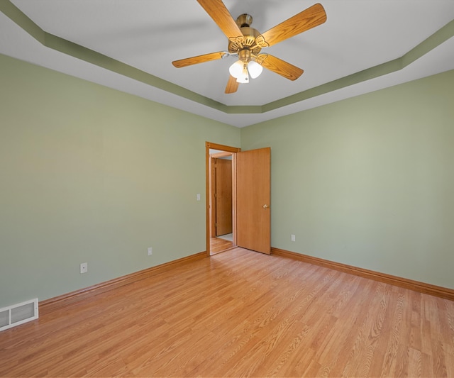 spare room with a raised ceiling, light wood-style flooring, baseboards, and ceiling fan