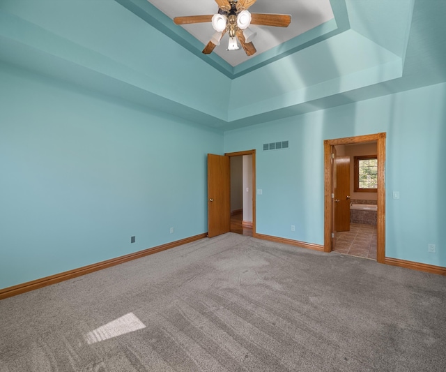 unfurnished bedroom featuring a raised ceiling, baseboards, carpet floors, ensuite bathroom, and ceiling fan