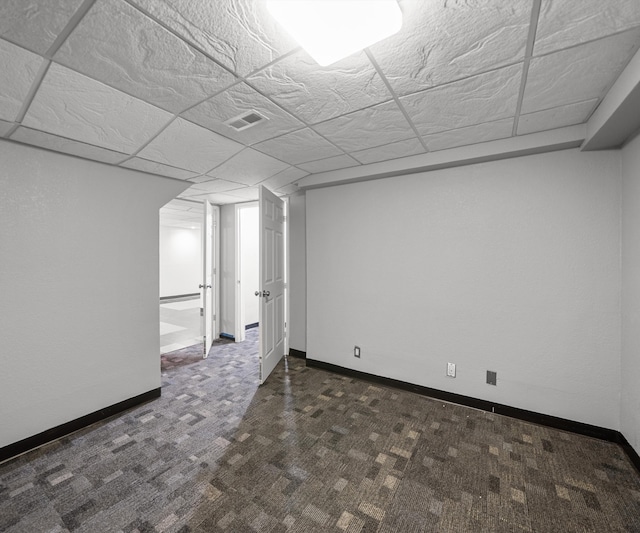 finished basement featuring dark carpet, baseboards, and a paneled ceiling