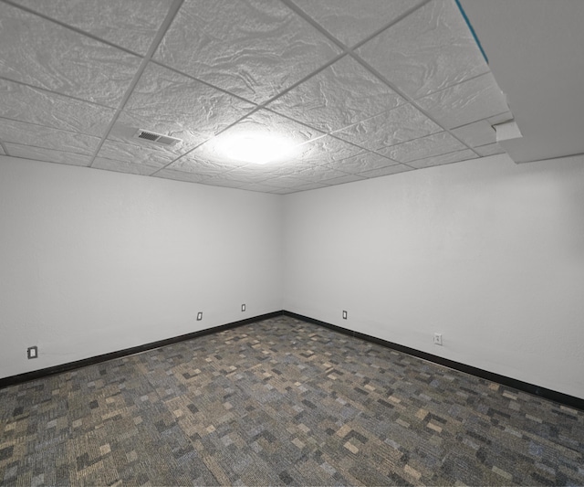 spare room featuring dark colored carpet, baseboards, and a drop ceiling