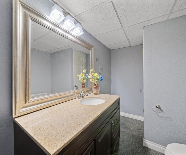 bathroom featuring a drop ceiling, vanity, baseboards, and toilet
