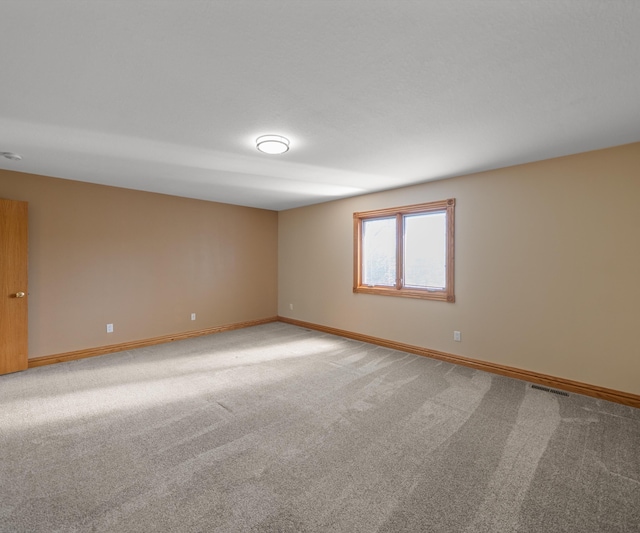 spare room featuring light carpet and baseboards