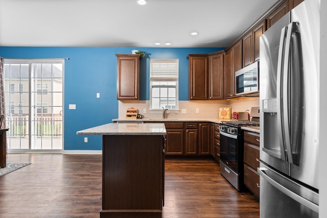 kitchen with appliances with stainless steel finishes, dark wood-style floors, a kitchen island, light stone countertops, and a sink