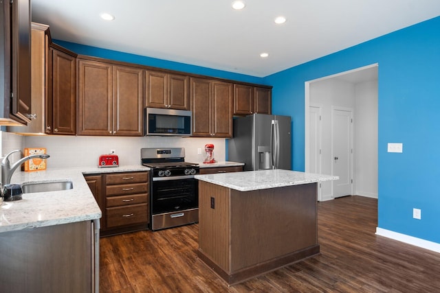 kitchen with appliances with stainless steel finishes, a sink, a center island, decorative backsplash, and dark wood-style floors