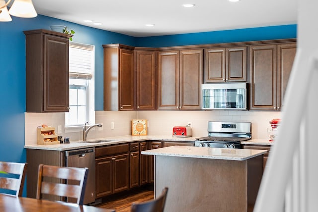 kitchen with stainless steel appliances, a sink, light stone countertops, backsplash, and recessed lighting