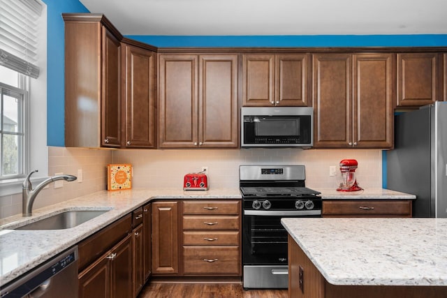 kitchen featuring stainless steel appliances, a sink, dark wood-style floors, light stone countertops, and tasteful backsplash