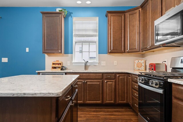 kitchen with stainless steel appliances, a sink, backsplash, light stone countertops, and dark wood-type flooring